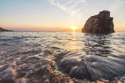 Scenic view of rocks in sea against sky during sunset