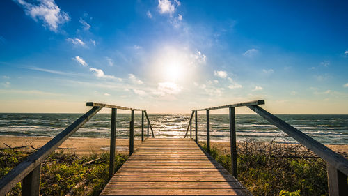 Boardwalk leading to sea against sky