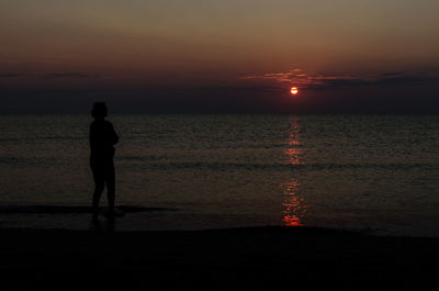 Silhouette woman standing at beach against sky during dusk