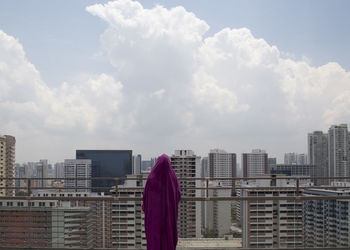 Rear view of woman standing by buildings against sky