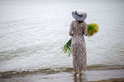 Rear view of a slide woman with a bouquet of wild flowers standing on the sea shore