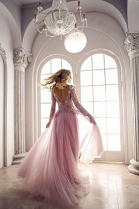 Beautiful young woman in pink lace dress spinning in the white room