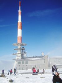 People by communication tower against sky during winter