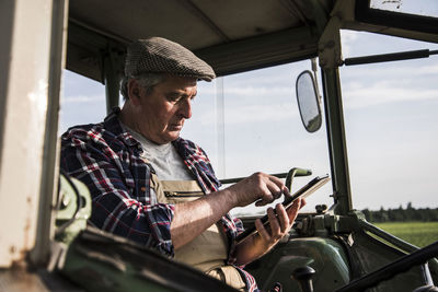 Farmer sitting in tractor using digital tablet