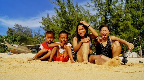 Portrait of happy sisters and brothers sitting on sandy beach