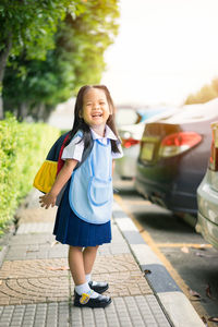 Portrait of cheerful schoolgirl standing on sidewalk