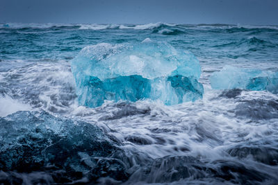 Close-up of wave splashing on shore against blue sky