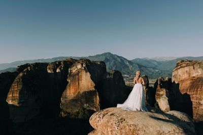 Rear view of bride standing on rock against sky