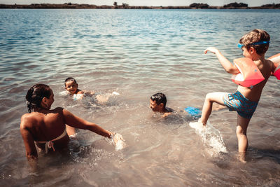 Happy mother and her sons playing in the water during summer day at the beach.