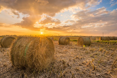 Hay bales on field against sky during sunset