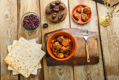 Jewish dish shuttle with meat in a clay dish on a wooden table near matzo and ingredients horizontal