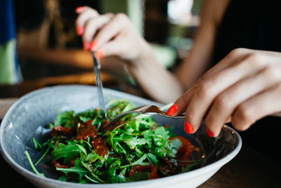 Cropped image of woman having salad from bowl in restaurant