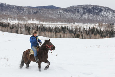 Full length of man riding horse on snow field