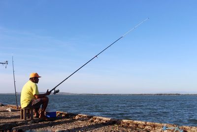 Man fishing by sea against clear sky
