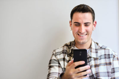 Young man with earphones smiling and looking at smartphone. chilling at home. copy space.