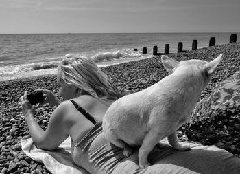 Dog sitting on woman at beach against sea