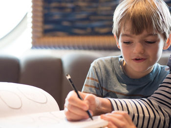 Cropped hands of sister drawing while sitting with brother at home