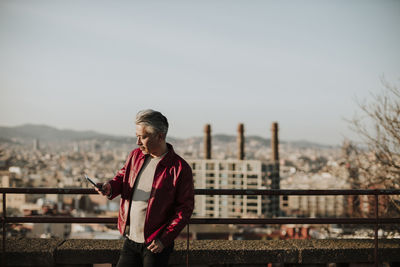 Full length of man standing on railing in city against sky