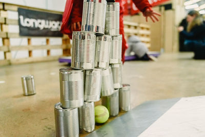 Midsection of child standing by stacked metallic containers with tennis ball on floor