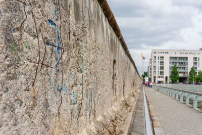 Footpath by wall against sky in city