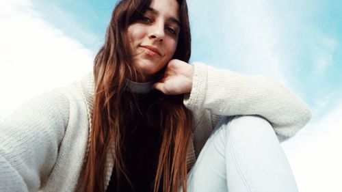 Low angle portrait of beautiful woman sitting against sky