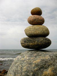 Stack of stones by sea against cloudy sky