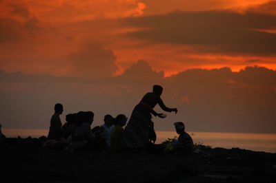 Silhouette people at beach against orange sky