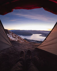 Low section of person on mountain against sky during sunset