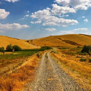 Dirt road amidst field against sky