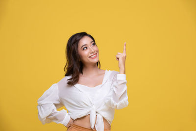 Portrait of smiling young woman against yellow background