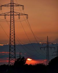 Low angle view of electricity pylon against sky at sunset