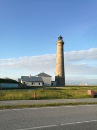 Lighthouse by road against sky