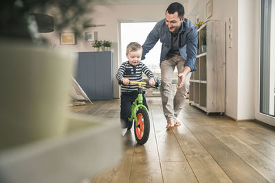 Father helping son riding with a balance bicycle at home