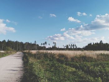 Road passing through field against cloudy sky