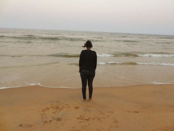 Rear view of woman standing on beach against sky