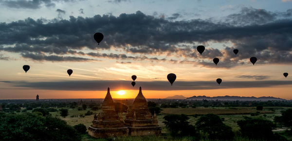 Silhouette hot air balloons flying over buddhist temples against sky during sunset
