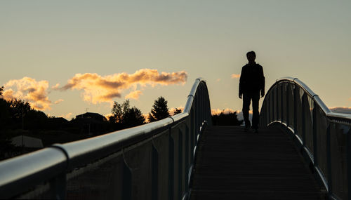 Rear view of man standing on footbridge against sky