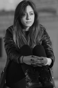 Sunlight falling on thoughtful young woman hugging knees while sitting outdoors