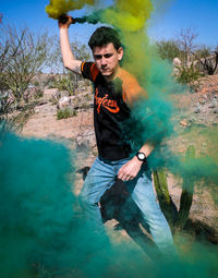 Portrait of young man holding camera while standing on land