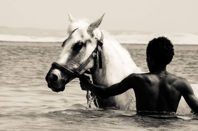 Man with horse in sea against sky