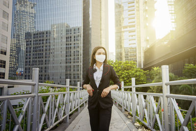Portrait of woman standing by railing against buildings in city