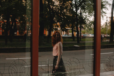 Woman looking at her reflection in glass window standing on street