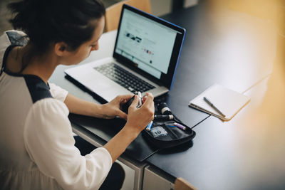 Businesswoman checking blood sugar level with glaucometer by laptop at desk