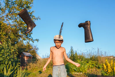 Shirtless boy with flying boots against sky
