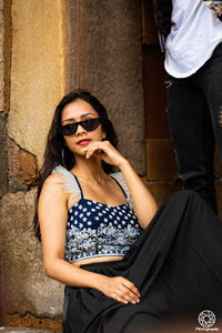 Beautiful young woman wearing sunglasses standing against wall