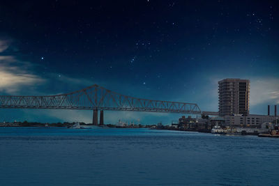 Illuminated bridge over river against sky at night