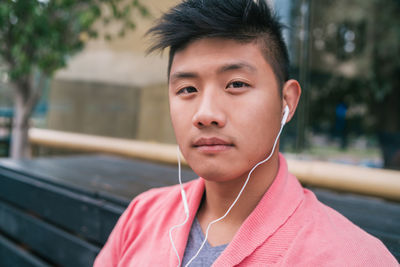 Portrait of young man sitting on bench while listening music