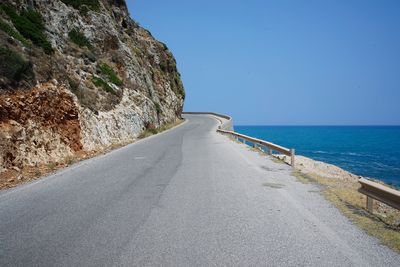 Road by sea against clear blue sky