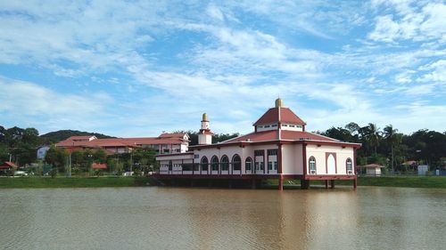 View of building by river against cloudy sky