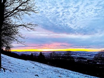 Snow covered land against sky during sunset